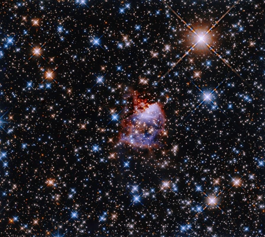 This Hubble image shows the star formation region G033.91+0.11. A central nebula lies in the center of a glittering backdrop of multicoloured stars. The nebula is reflecting light from a bright and massive young protostar. Scientists use the initial mass function to estimate the mass ratios of stars created in such starbirth regions. Image Credit: NASA, ESA, and R. Fedriani (Instituto de Astrofisica de Andalucia); Processing: Gladys Kober (NASA/Catholic University of America)