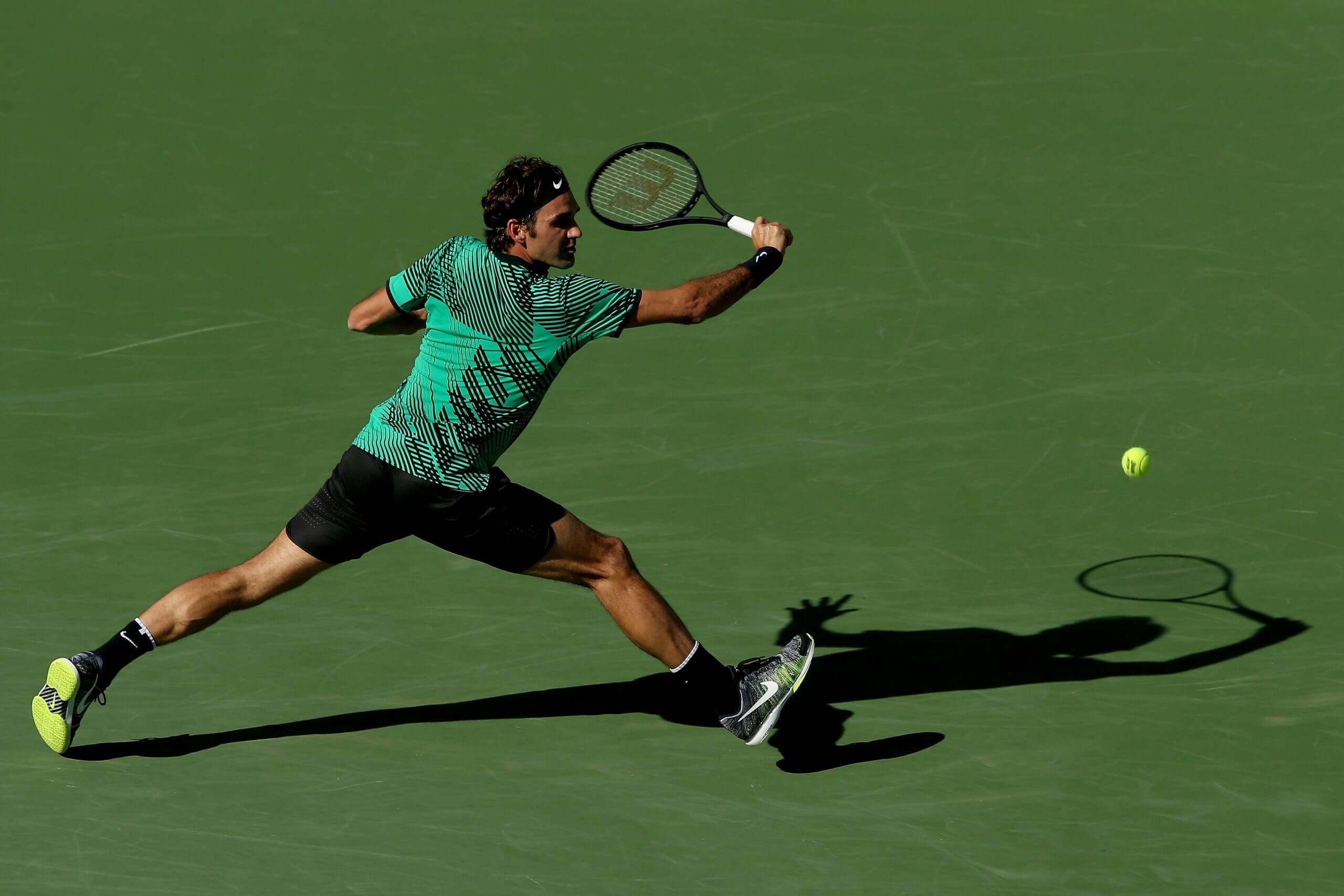 Roger Federer reaches out to hit a slice backhand on a green tennis court.