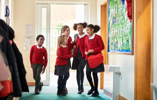 Group of female friends chatting in school corridor, carrying bags, wearing school uniform