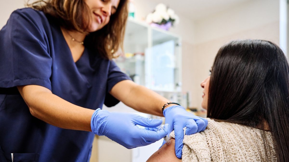 Rear view of a young woman receiving an injection for flu in an hospital - healthcare and medical insurance concept