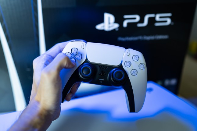 Hand holding a DualSense controller in front of a PS5 logo