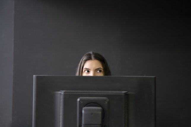 Office Worker Sneaking a Peek Above Laptop in a Modern Workspace During Daytime, hiding from boss