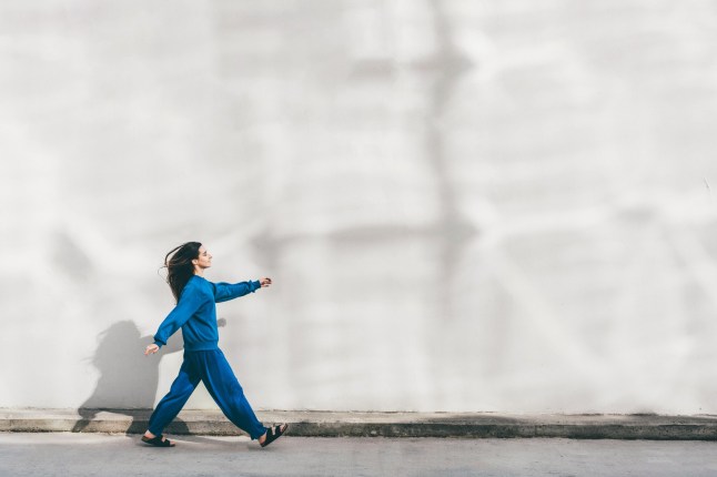 Young woman walking against a wall.