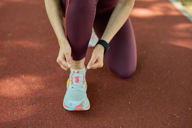 Woman kneeling on an outdoor running track tying her shoe before a run.
