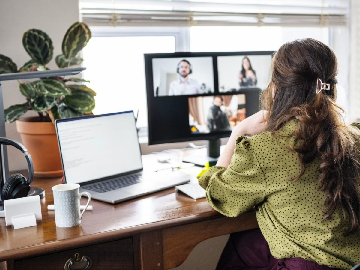 Rear view of woman having a video call meeting with business team on desktop computer while working remotely from home