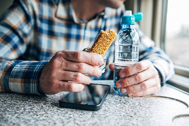 healthy snack on the go, man's hand holding cereal bar and bottle of water on train during trip