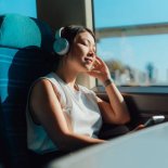 Young Asian woman with eyes closed, listening to music with wireless headphones in train. Business and leisure travel. Travel and vacation.