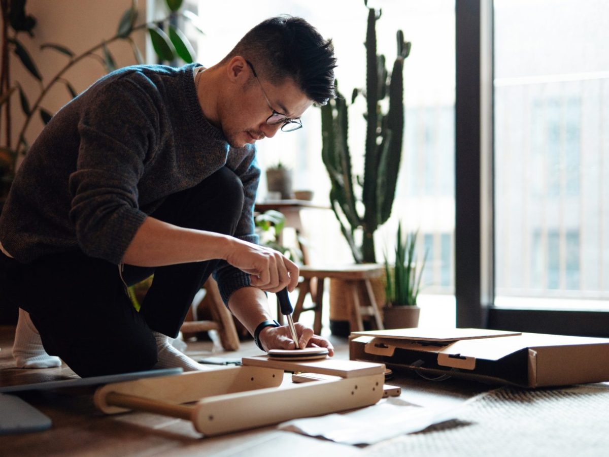 Young Asian man assembling furniture with screwdriver, setting up new home. Doing DIY at home.