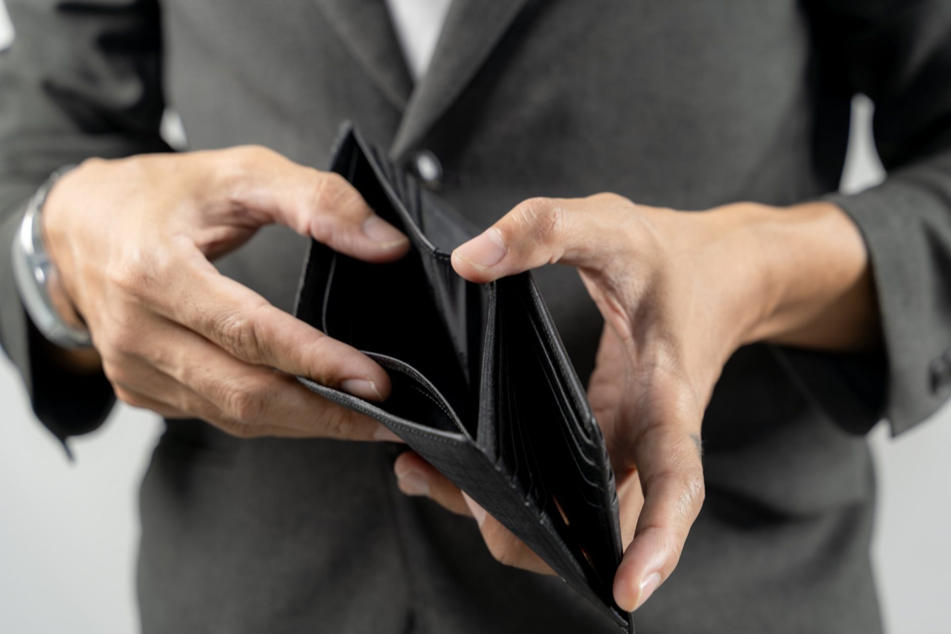A close-up shot of a young man's hands opening an empty leather wallet, symbolizing financial struggle, poverty, and money problems.