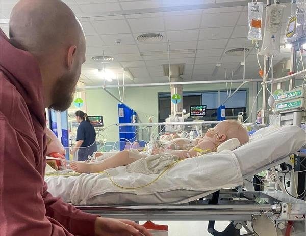 Florence Wilde, in hospital with her father Dom. // A toddler whose belly ballooned was diagnosed with a 2kg tumour after doctors repeatedly told her parents she was constipated. Florence Wilde, two, was diagnosed with neuroblastoma - a rare cancer of the cell - in November 2024. Her parents Anna Chattaway and Dom Wilde, both 32, first noticed something was wrong when Florence became repeatedly rundown. The toddler's tummy began to swell so the pair rushed her to Three Villages GP in Stourbridge but doctors ruled out the symptoms as constipation, prescribing the tot laxatives. Photo released 21/08/2026