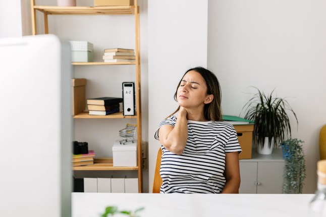 Young Latin American woman working from home suffering neck pain, massaging her neck while sitting at her desk