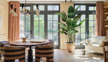 Dining area with brown and blue striped tub chairs, round pedestal table, black Crittall-style doors, apricot curtains, white armchairs, large potted plant and multi-light pendant
