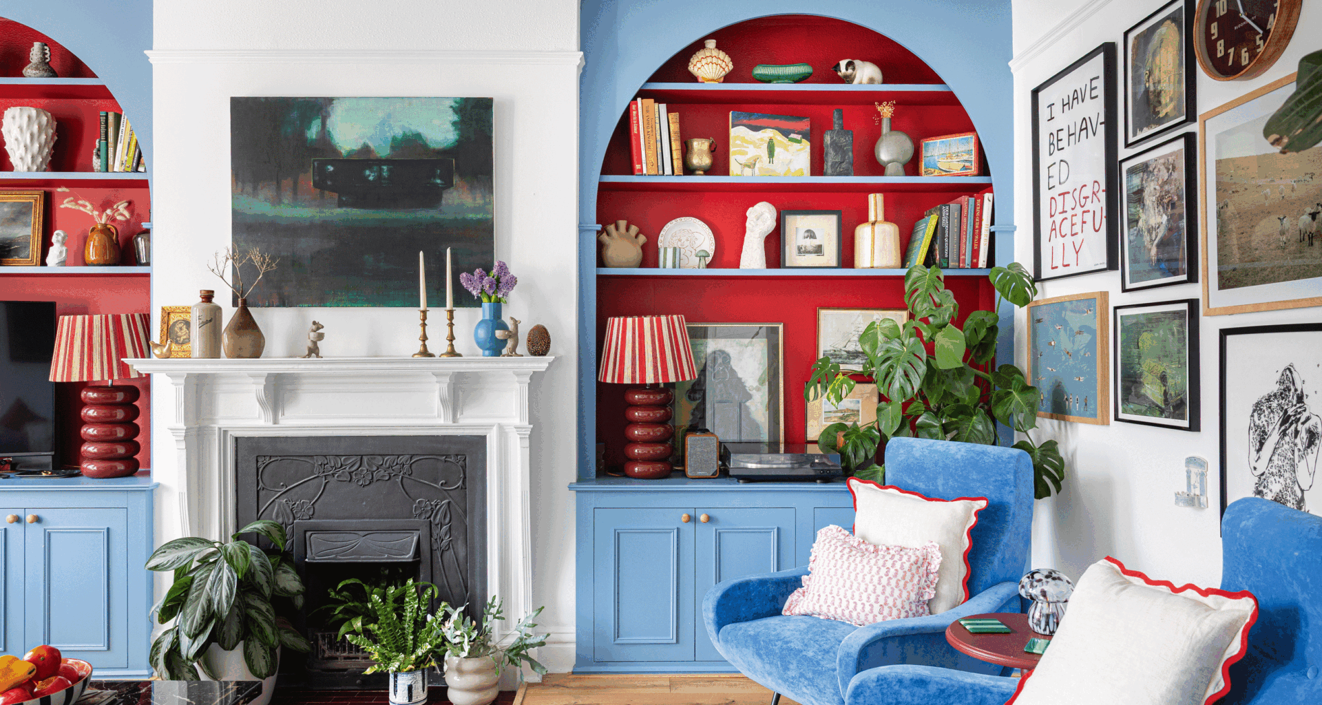 a living room with bright blue painted alcove shelving with bold contrasting red recessed shelves with a gallery wall, fireplace and plenty of colour