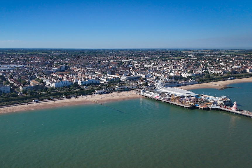 A photo of a coastline, showing a pier and amusement park in the right corner and suburbs stretching inland in the distance