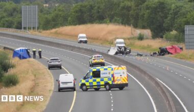 A shot of a car crash site showing a section of closed motorway with many emergency service vehicles on the road and debris from the crash.