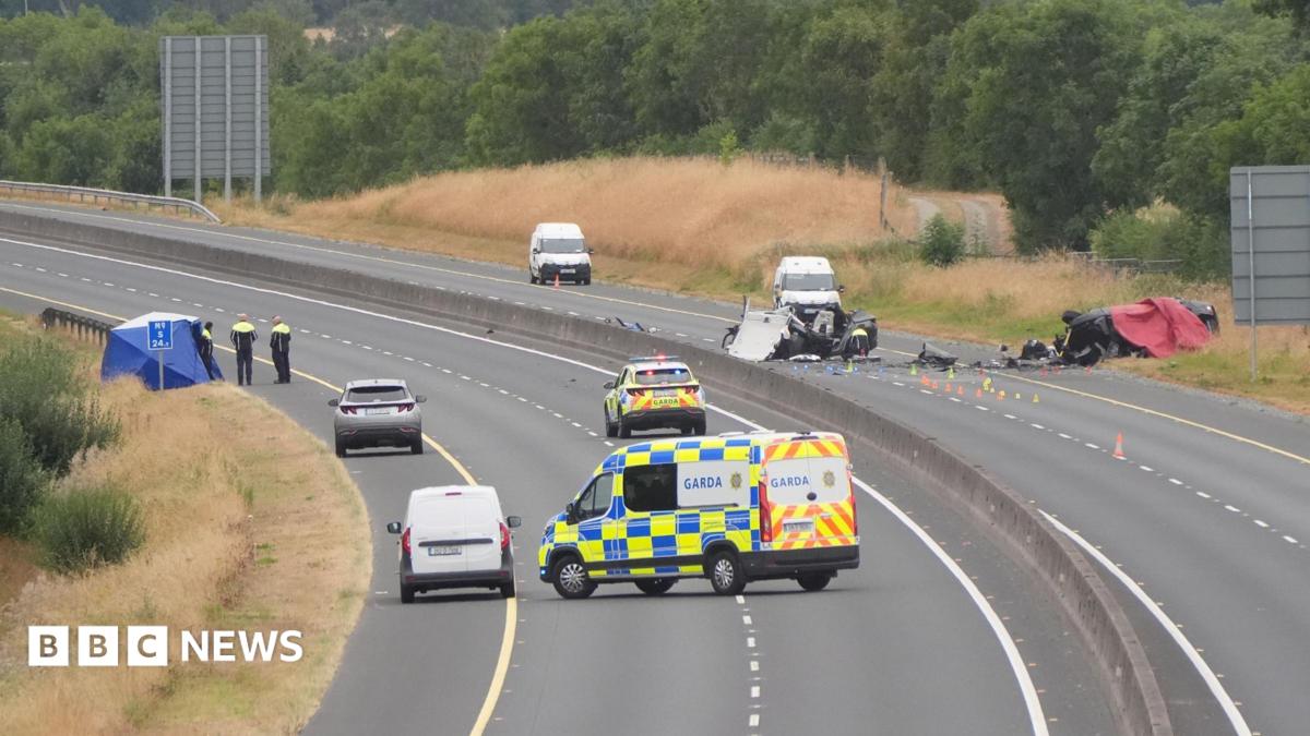 A shot of a car crash site showing a section of closed motorway with many emergency service vehicles on the road and debris from the crash.