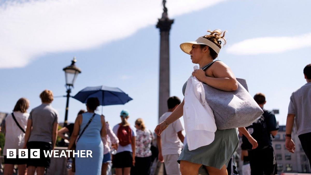 A woman with a sunhat and visor on walks through Trafalgar Square with other people holding umbrellas in the background to shield them from the sun. With Nelson's Column in the background