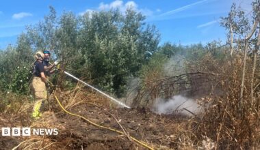 Photograph of a firefighter tackling a blaze at an illegal waste sump in Ashton-upon-Mersey. The image shows a jet of water being fired at the ground.