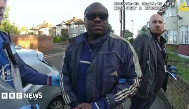 Simon Levy pictured after being arrested by police. He is wearing sunglasses and a blue sports jacket outside a building.