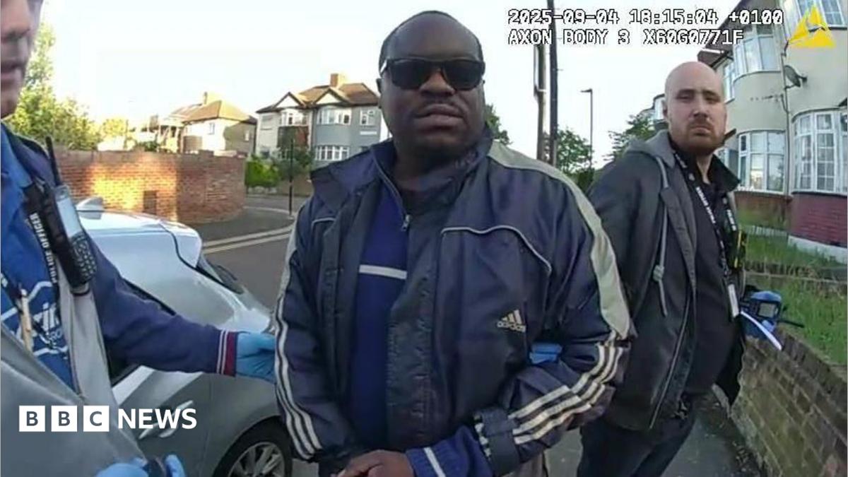 Simon Levy pictured after being arrested by police. He is wearing sunglasses and a blue sports jacket outside a building.
