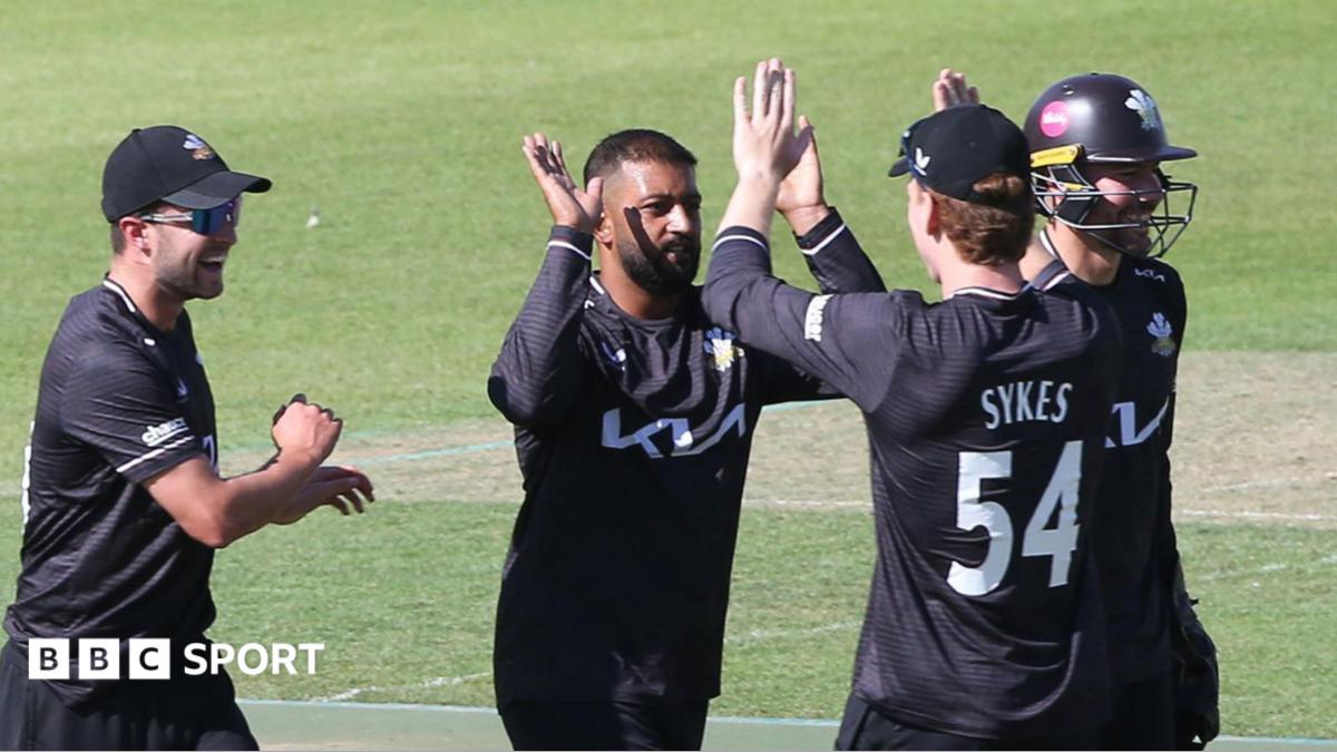Ryan Patel raises his bat to the crowd after scoring a half-century. He is wearing an all black Surrey One-Day Cup kit