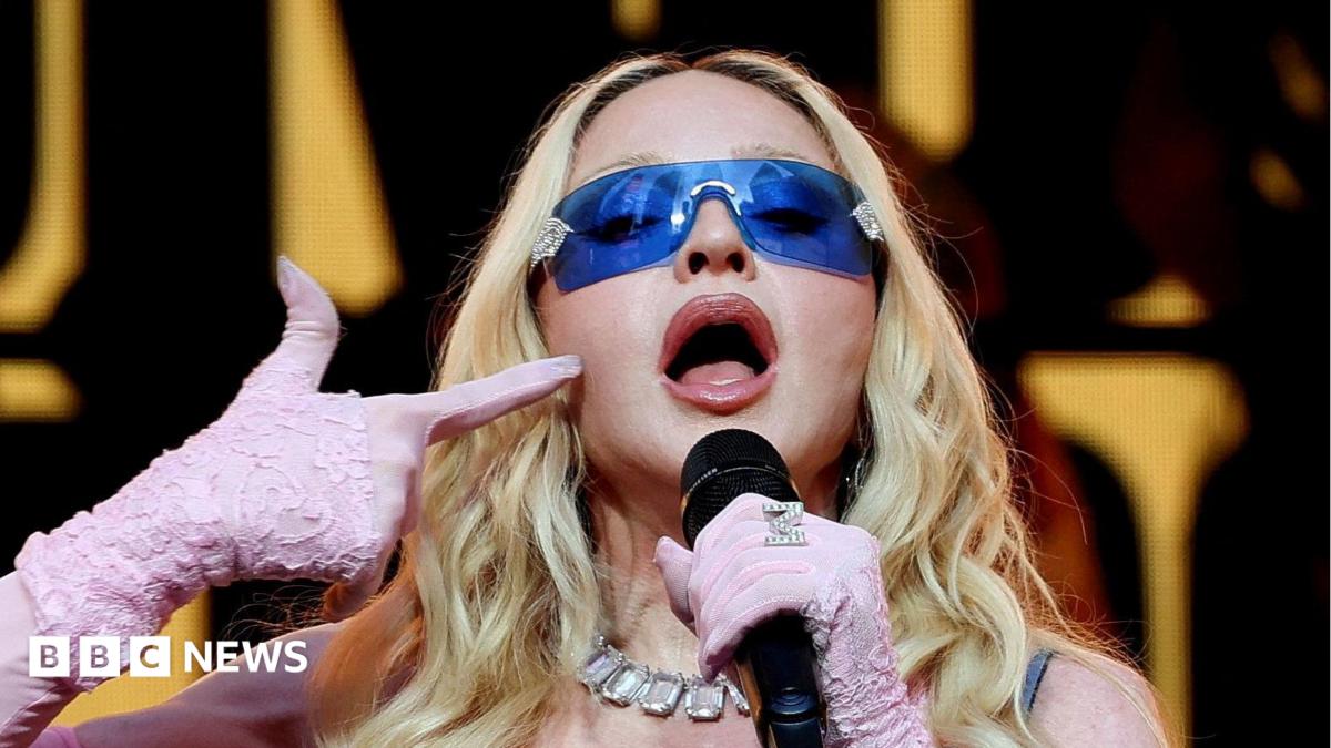 Madonna, wearing purple sunglasses and pink gloves, performing during a surprise concert in Times Square in New York City in June