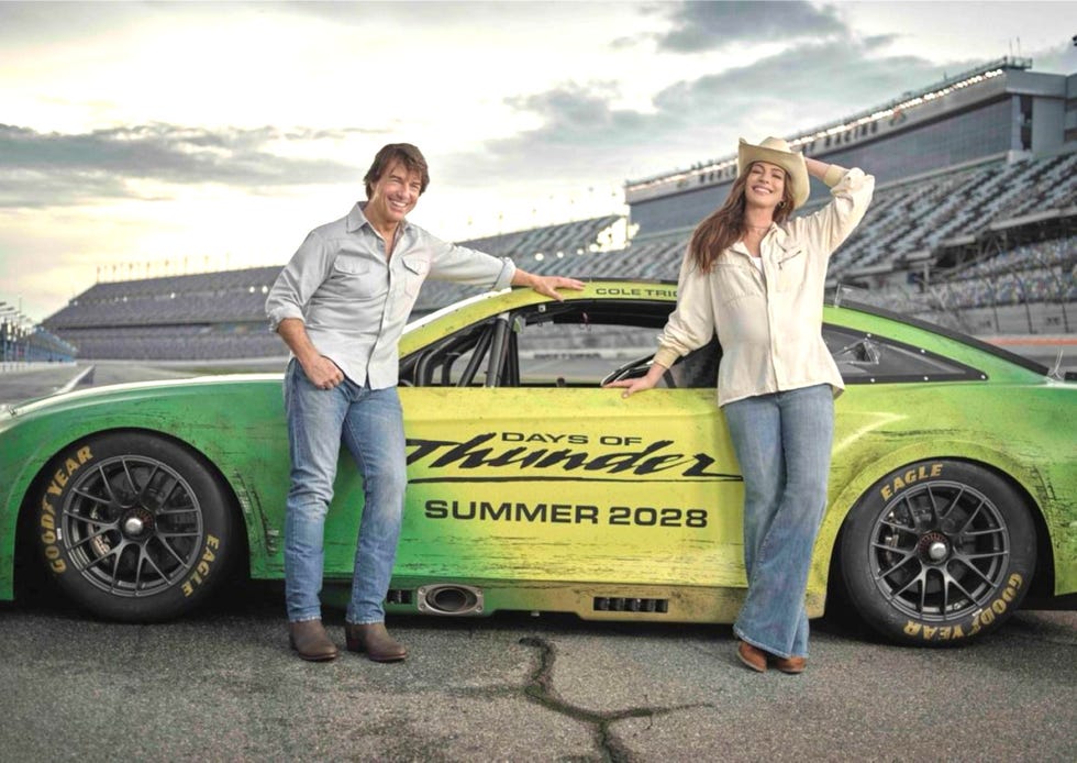 days of thunder 2 tom cruise anne hathaway two people smiling beside a "days of thunder" race car on a track.