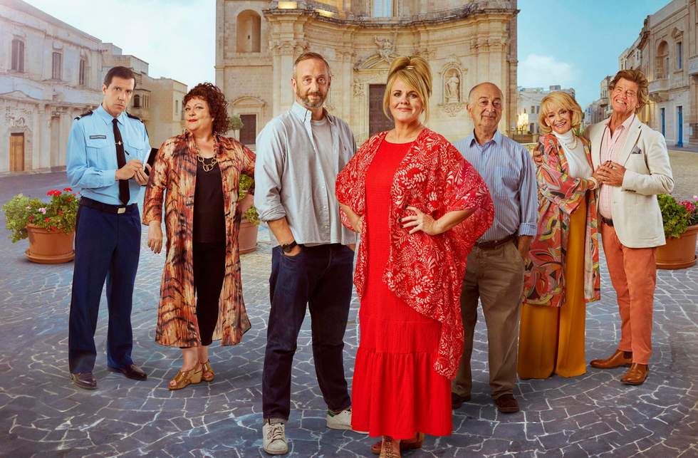 The Madame Blanc mysteries group of seven people standing in a cobblestone square with historic buildings in the background