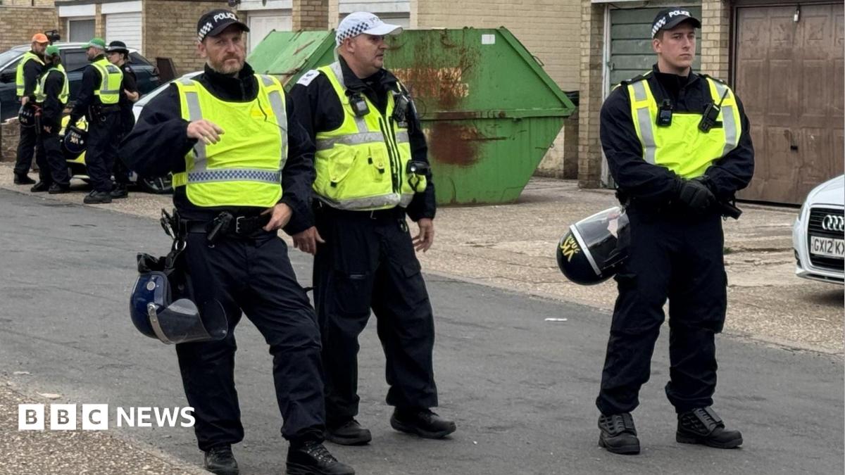 Three police officers are pictured standing in a road. They are wearing yellow vests and all have caps on