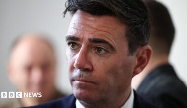 Andy Burnham wearing a black suit and white shirt, looking to the left of the frame of the photograph. The picture is a close up with most of Burnham out of shot bar his head and shoulders.