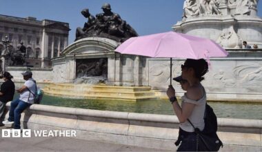 two people under an umbrella shading themselves from the strong summer sunshine walking in front of a fountain at Buckingham Palace