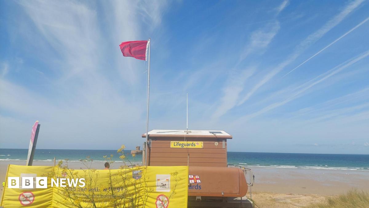 A picture of a beach with a large red flag flying.