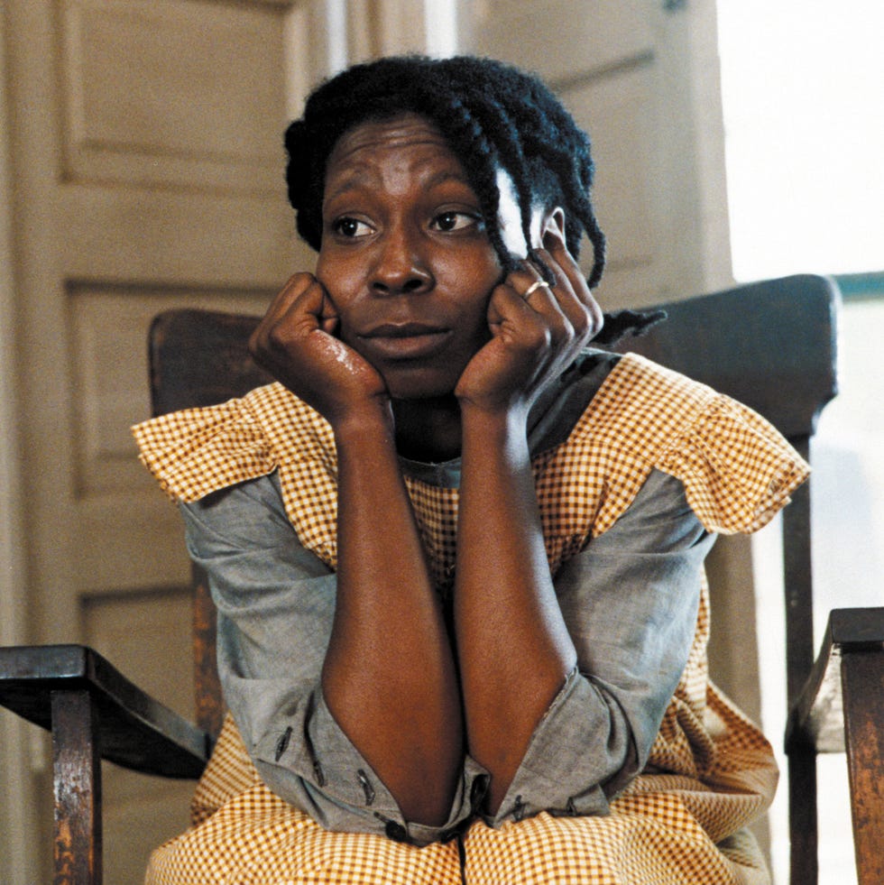 a woman sits on a chair, resting her chin on her hands, looking contemplative.