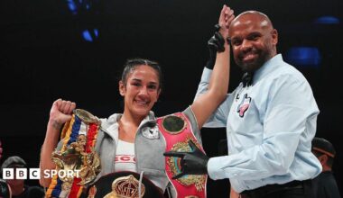 Amanda Serrano has her arm raised by a referee and is celebrating with her belt