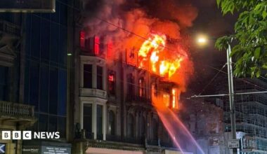An old Victorian building on fire with jets of water directed at the flames. The photo is taken at night.