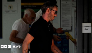 Jack Tweed leaves Chelmsford Magistrates' Court. He is in a black T-shirt and wearing black sunglasses. He has a beard and tattoos of a star on one arm and writing on the other.