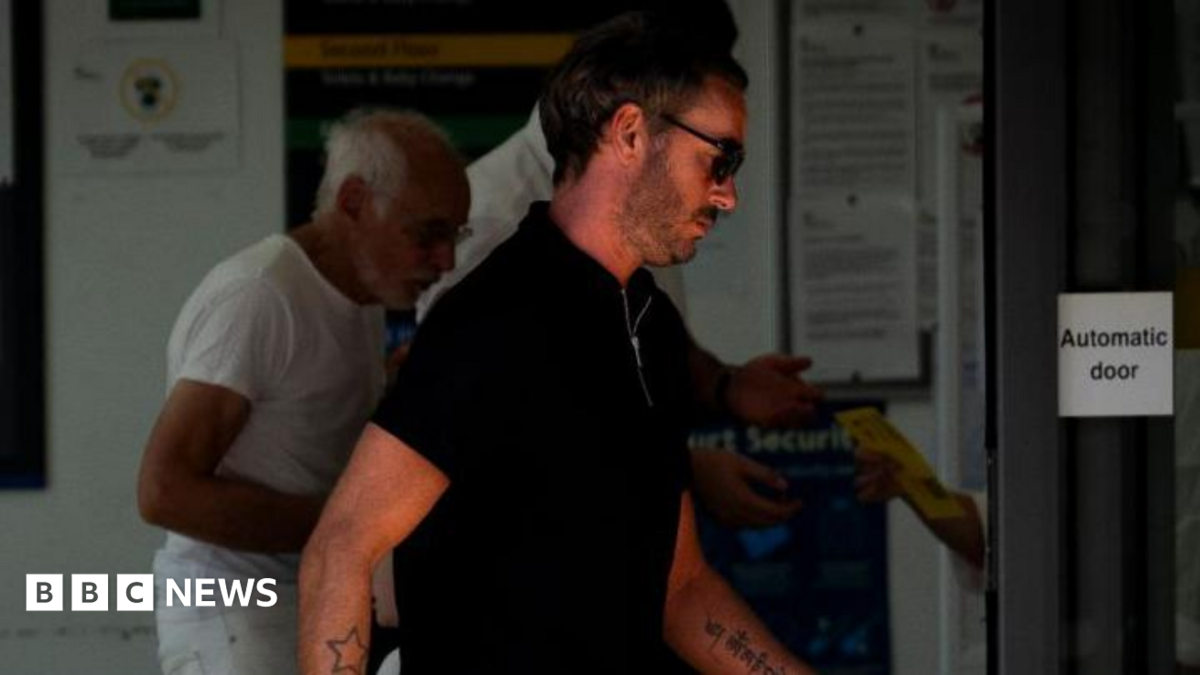 Jack Tweed leaves Chelmsford Magistrates' Court. He is in a black T-shirt and wearing black sunglasses. He has a beard and tattoos of a star on one arm and writing on the other.
