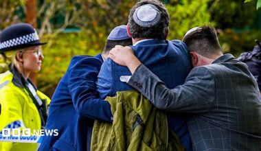 Worshippers console each other after the attack o0n their synagogue while a police officer looks on.