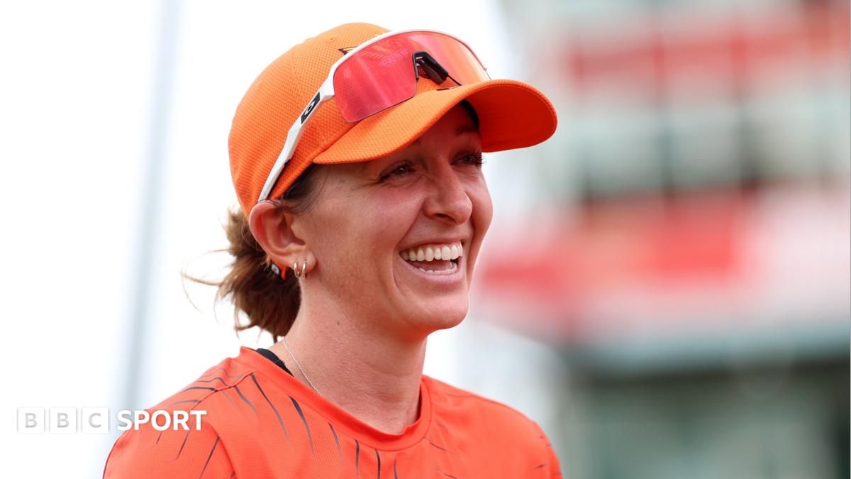 Kate Cross smiles, while wearing orange Sunrisers Leeds kit