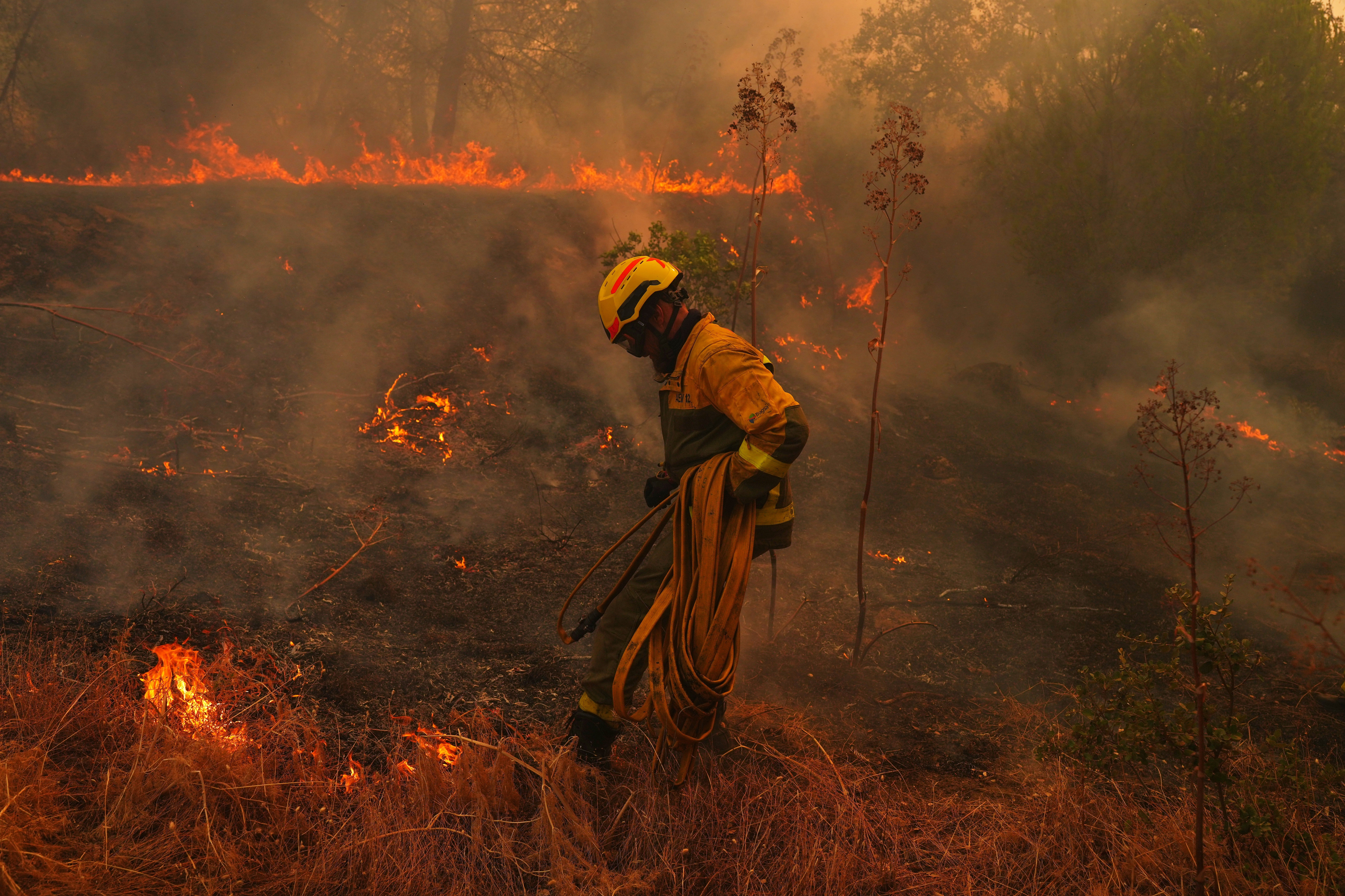 A firefighter carries a hose while battling a wildfire in San Martin de Valdeiglesias, west of Madrid, Spain