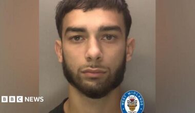 A police mugshot of a man with dark hair and a short beard