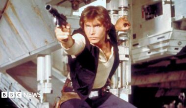 Han Solo in a screen grab from Star Wars. He has a phaser in hand about to shoot and is holding the open exit ramp to the millennium falcon