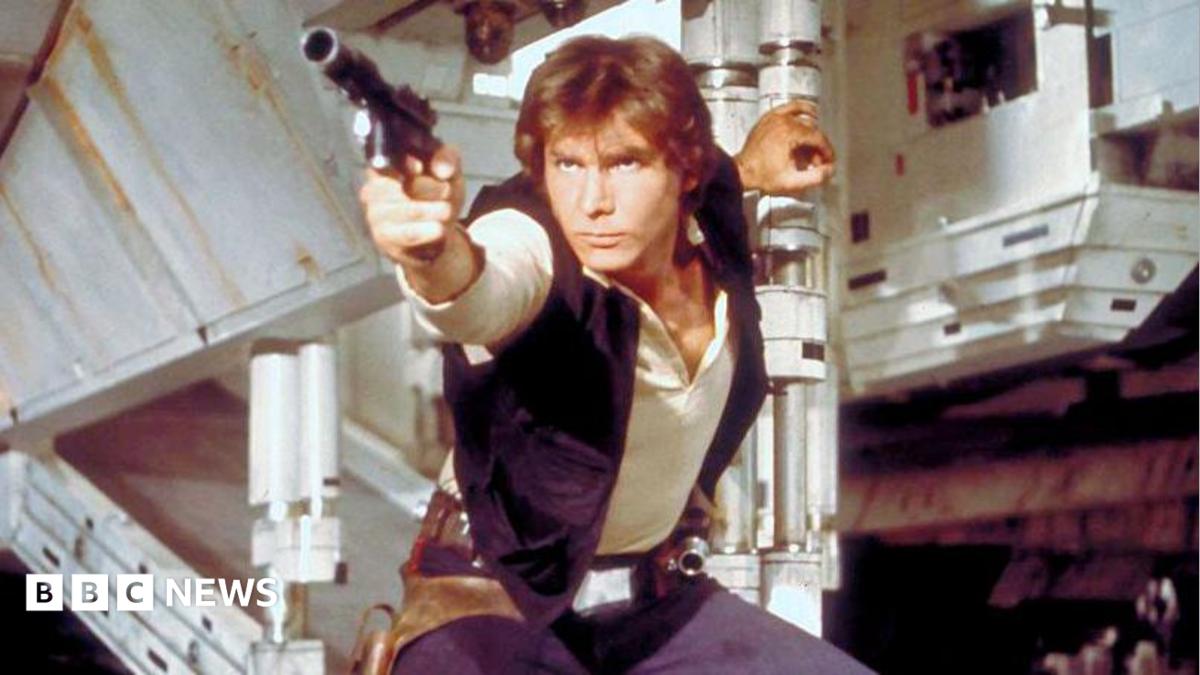 Han Solo in a screen grab from Star Wars. He has a phaser in hand about to shoot and is holding the open exit ramp to the millennium falcon