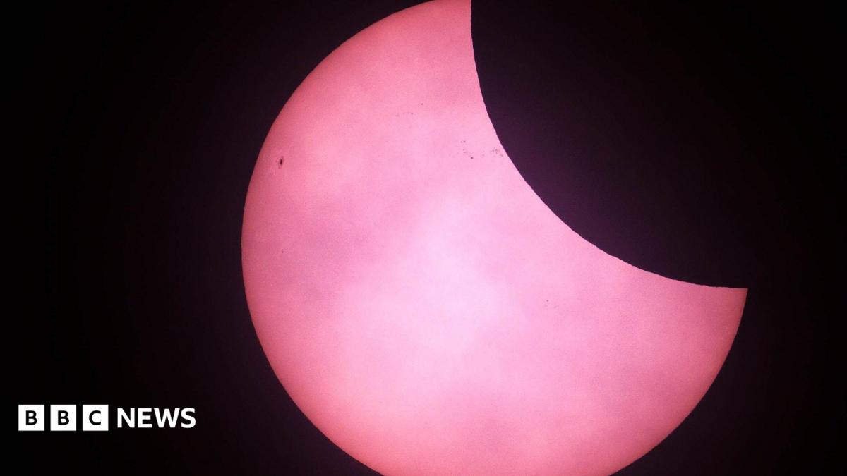 The top right corner of the sun has been obscured by the moon which appears black. The sun appears pink in the picture from St Martins in 2025.