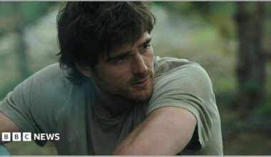 Jacob Elordi appears dishevelled with shaggy hair, a beard and wearing a light green t-shirt.