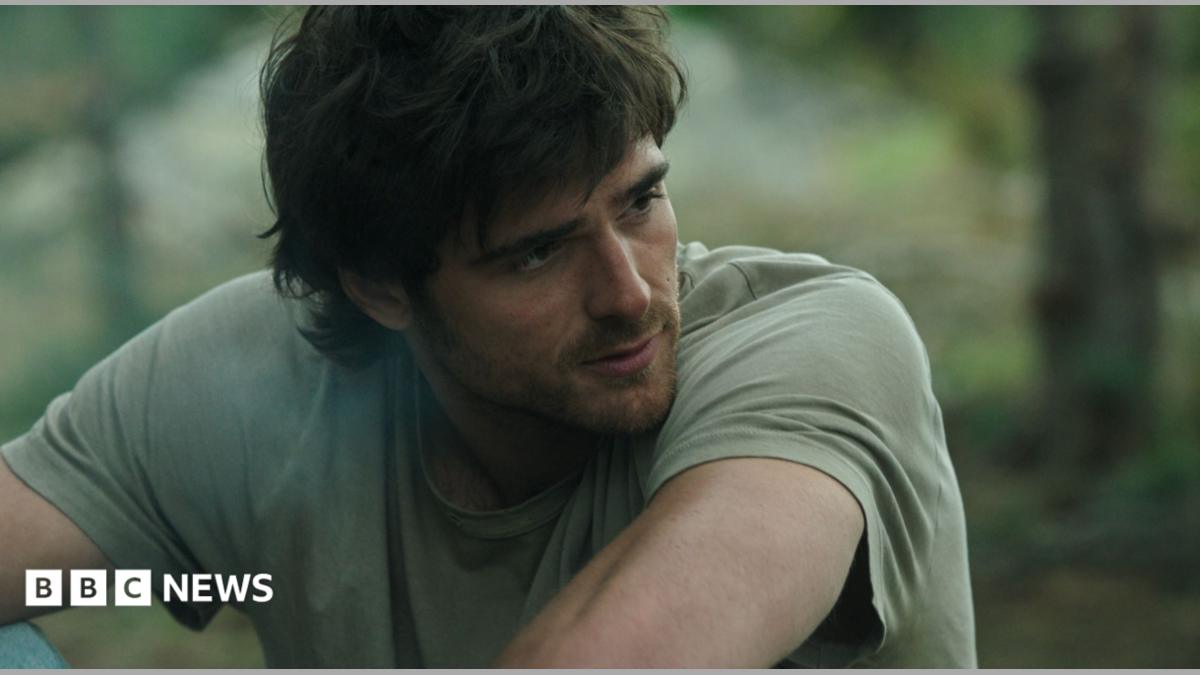 Jacob Elordi appears dishevelled with shaggy hair, a beard and wearing a light green t-shirt.
