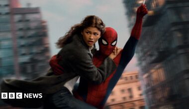 Spider-Man swings through the city on web whilst holding MJ, played by Zendaya.