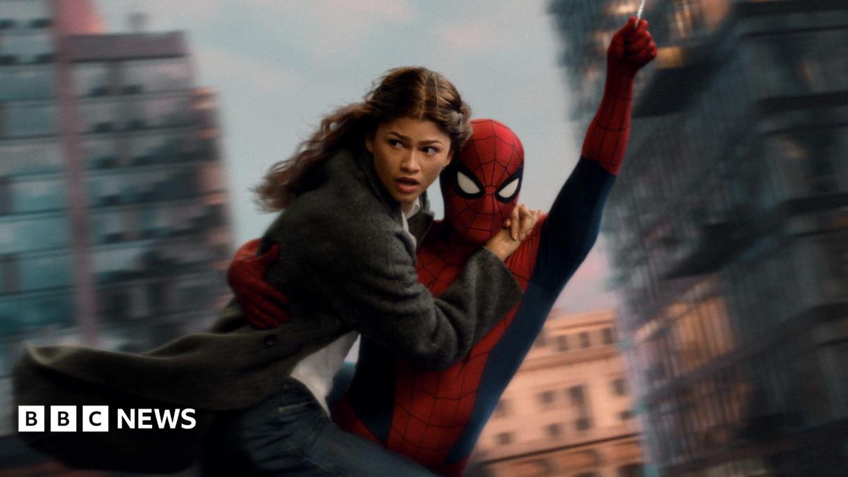 Spider-Man swings through the city on web whilst holding MJ, played by Zendaya.