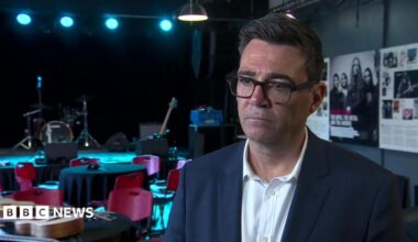 Andy Burnham. He has dark hair, wearing glasses, a navy blazer and white shirt.