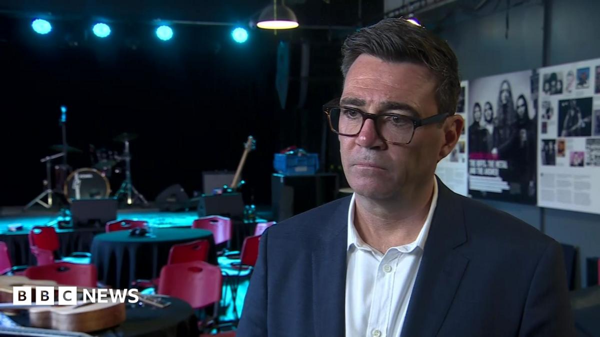 Andy Burnham. He has dark hair, wearing glasses, a navy blazer and white shirt.